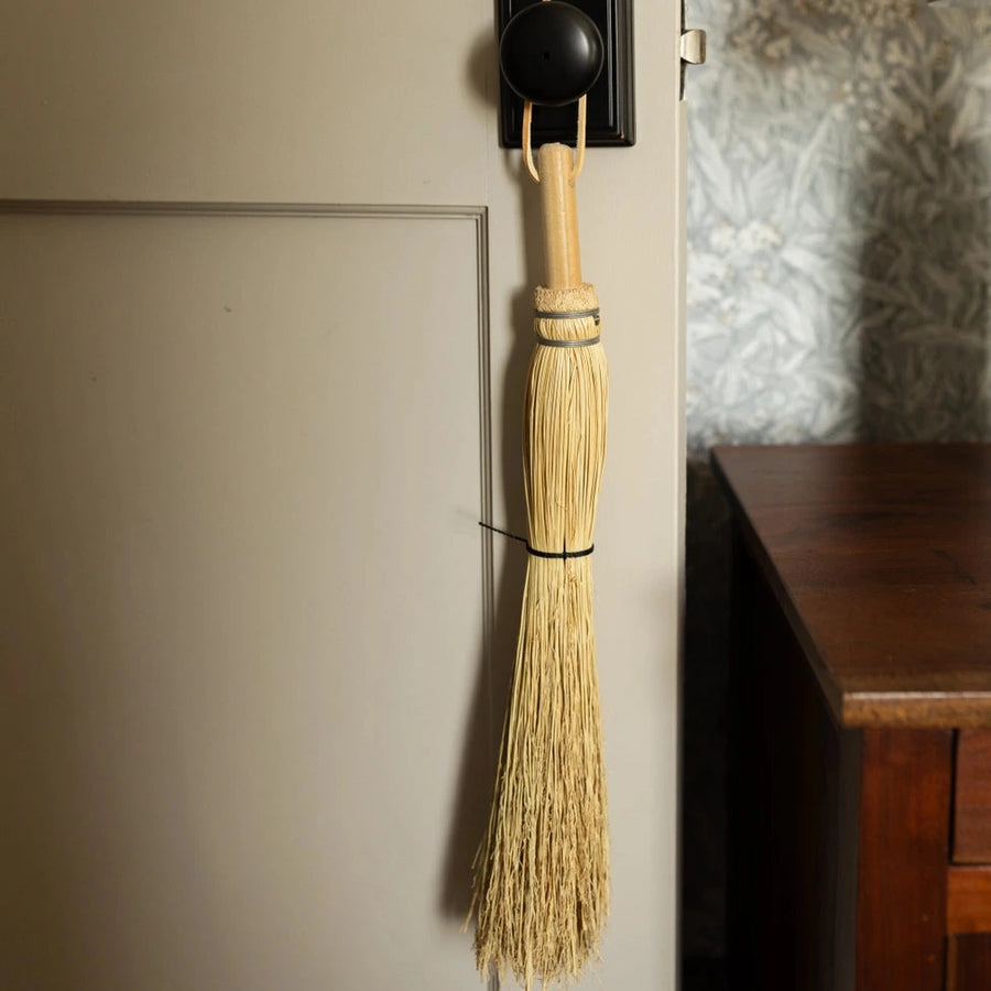 Broom hanging on a door handle against a neutral wall.