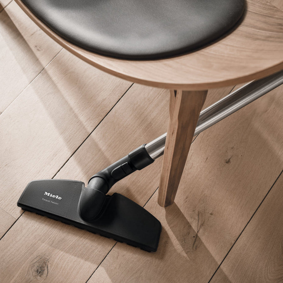 Miele vacuum cleaner head on a wooden floor with a chair in the background