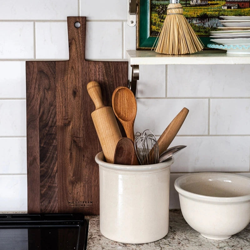Kitchen counter with wooden utensils in a white container, a cutting board, and a bowl.